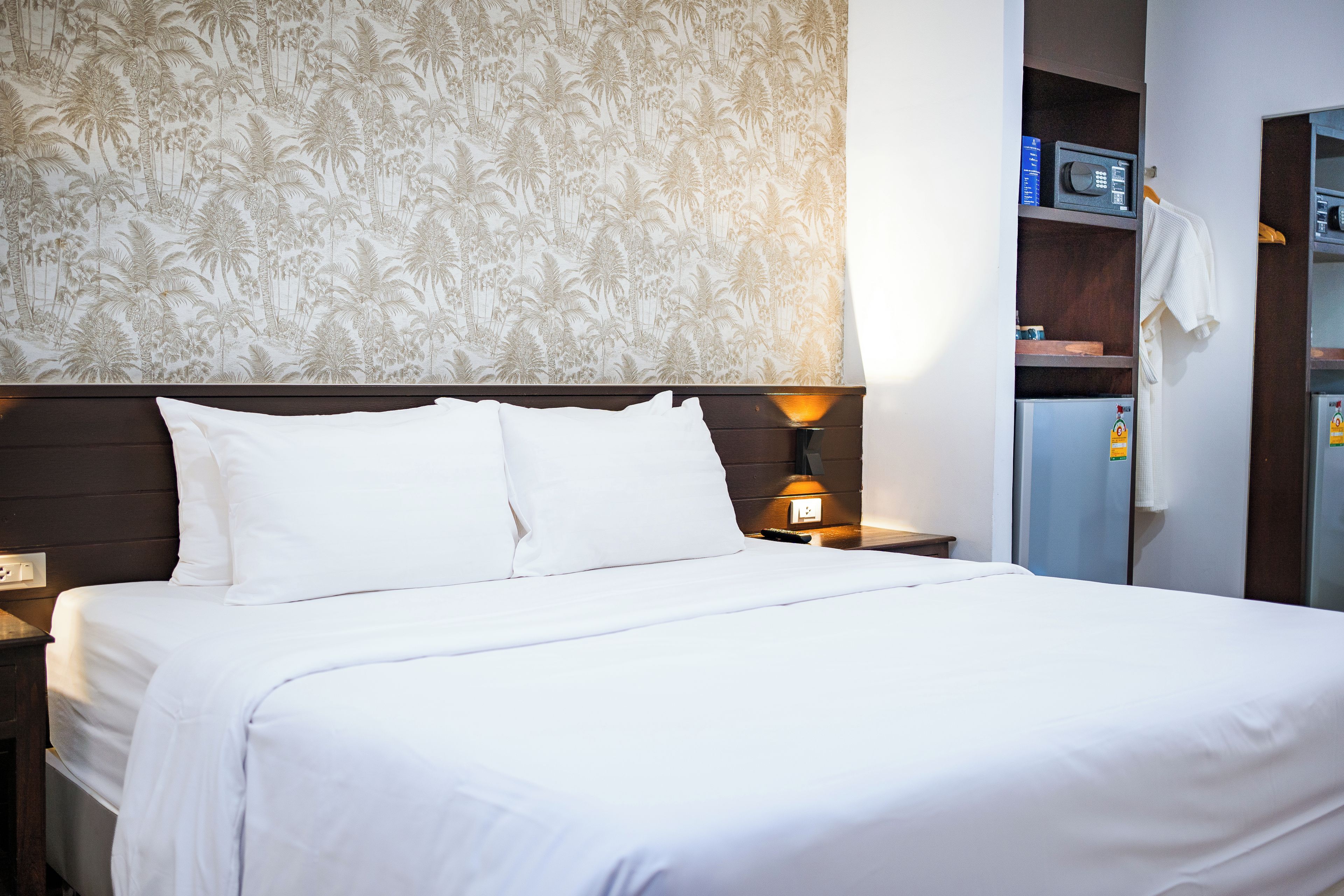 Ein Hotelzimmer mit einem großen Bett, einem Nachttisch mit Lampe, einem Kleiderschrank und einer Minibar.