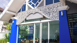 Een gebouw met een blauwe gevel, grote glazen deuren en een decoratieve witte metalen balustrade boven de ingang.