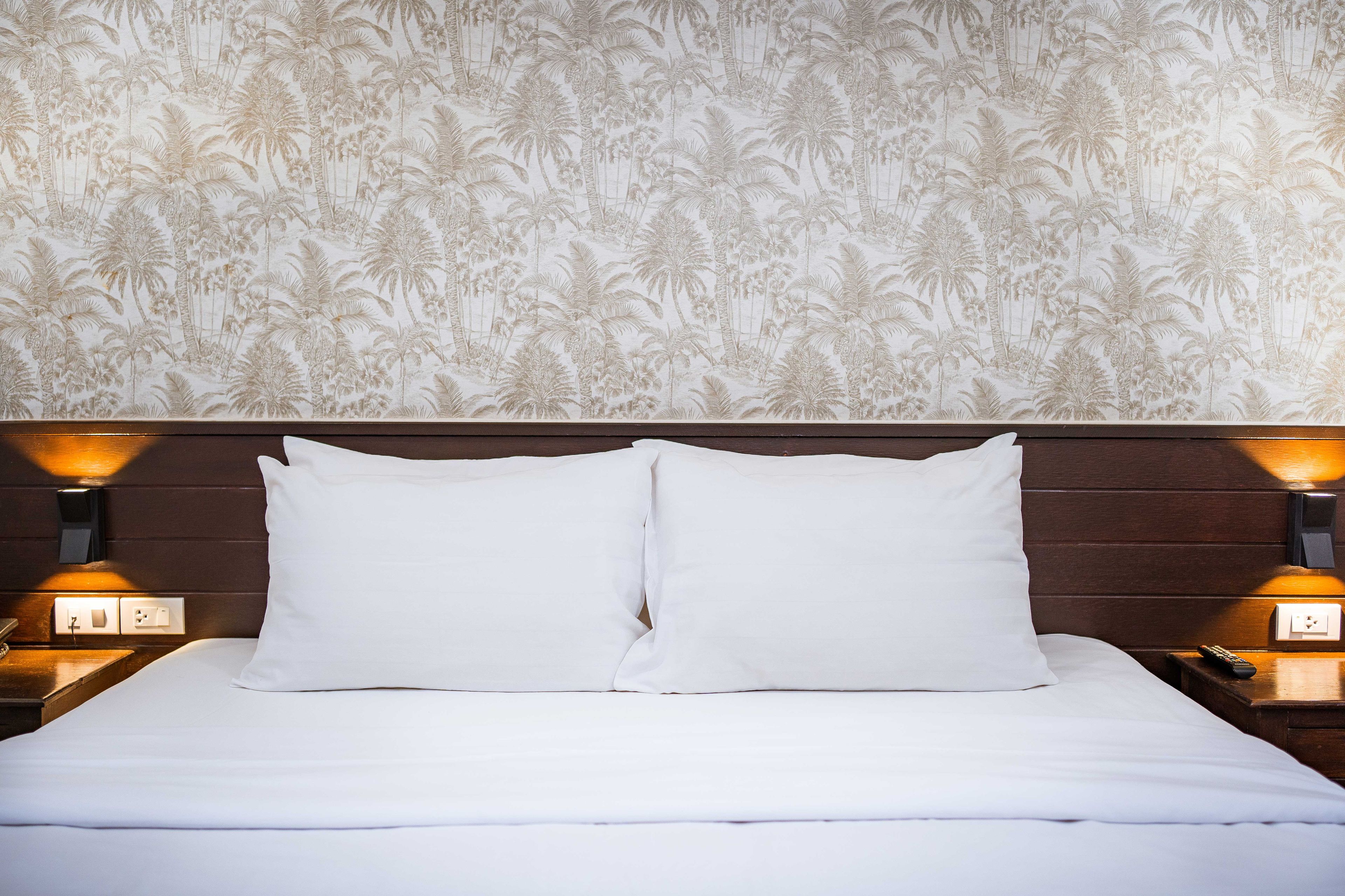 Una habitación de hotel con una cama, dos lámparas de noche y una pared con un diseño tropical.