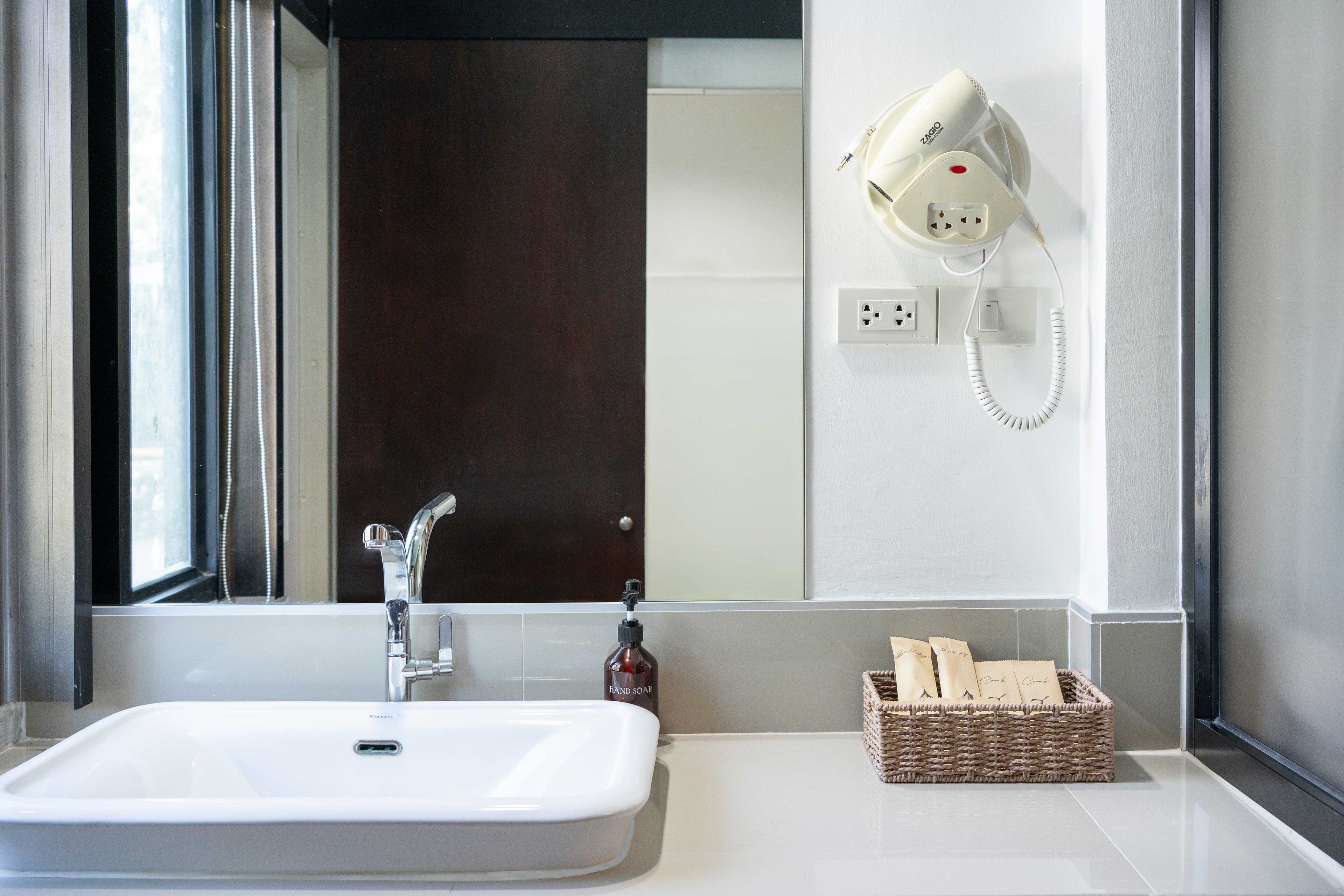 A bathroom with a white sink, a hairdryer on the wall, a bottle of hand soap, and a basket of towels.