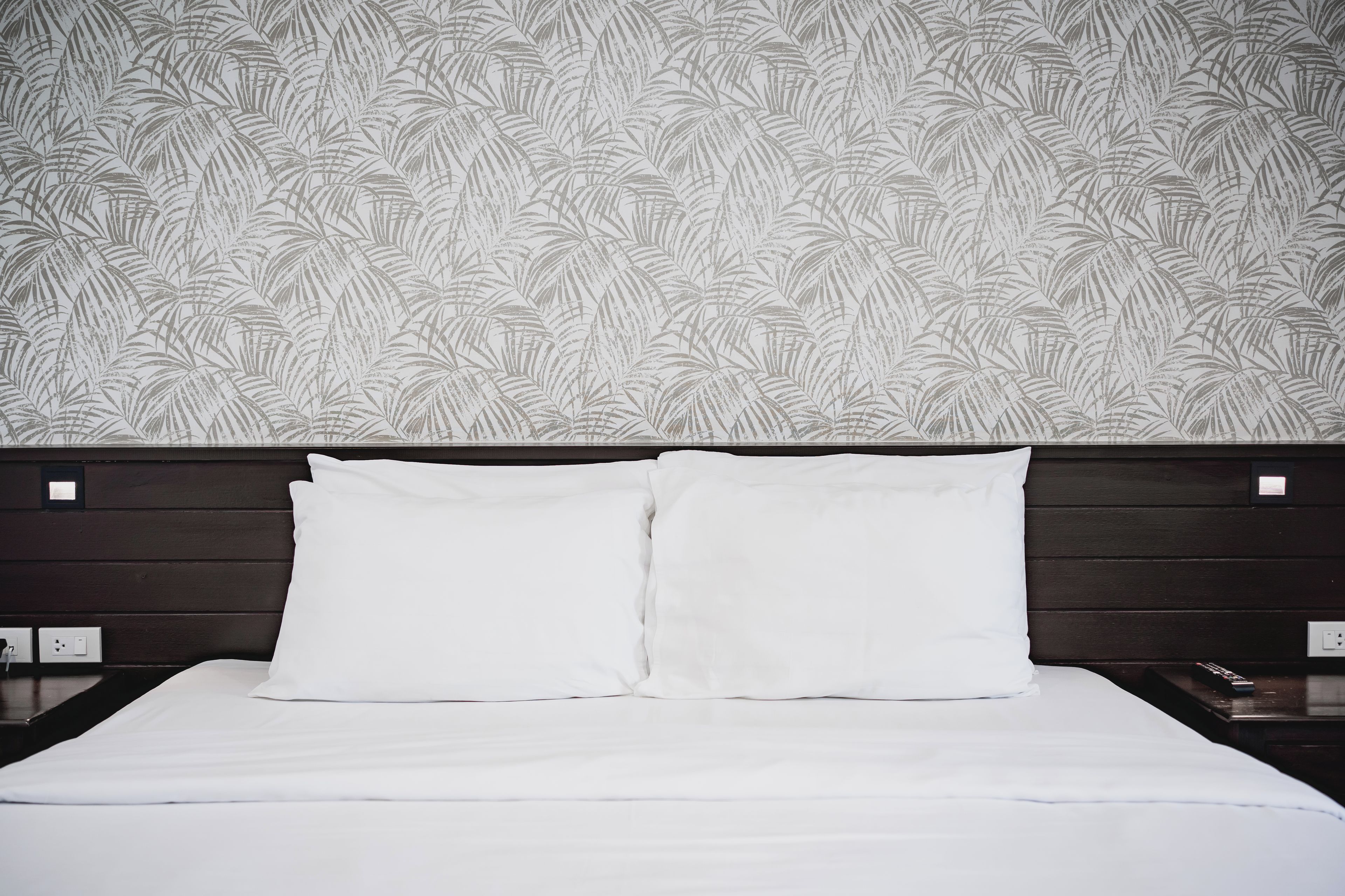 Une chambre d’hôtel avec un lit, du linge de lit blanc et un papier peint à motifs.
