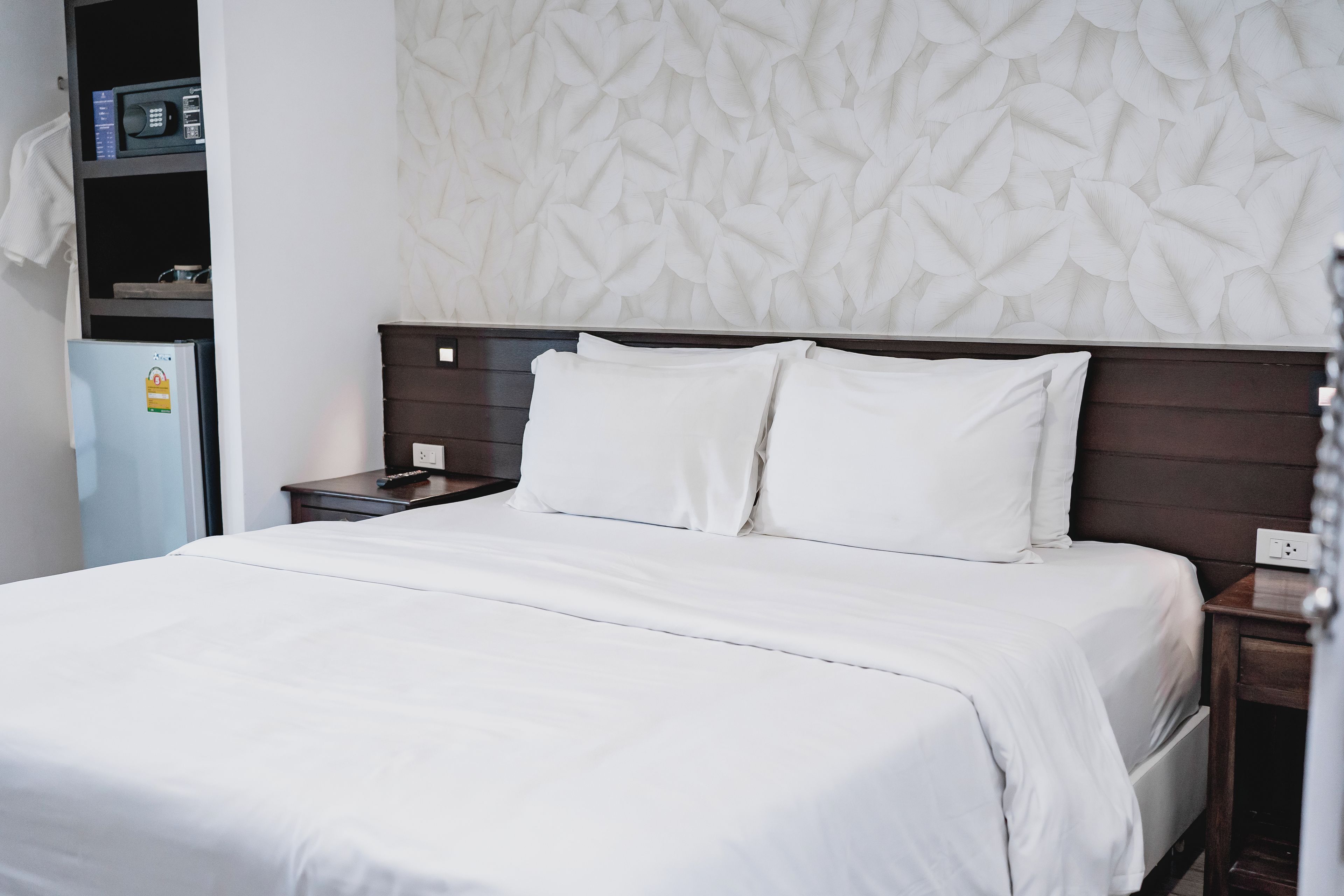 A hotel room with a bed, a nightstand, a wall-mounted telephone, and a shelf with a remote control.