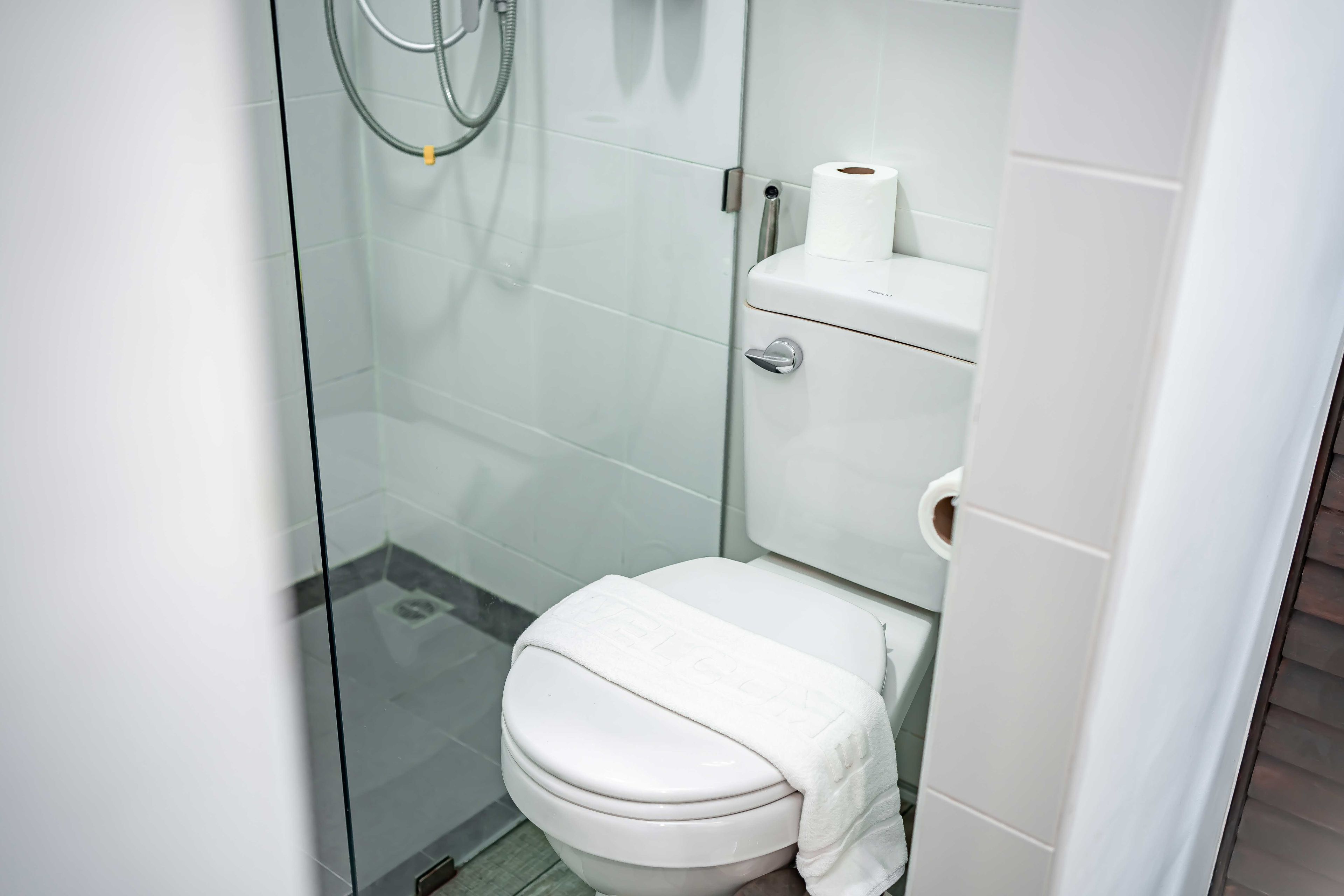 Ein kleines, modernes Badezimmer mit einer Duschkabine aus Glas, einer Toilette und einer Toilettenpapierrolle an der Wand.