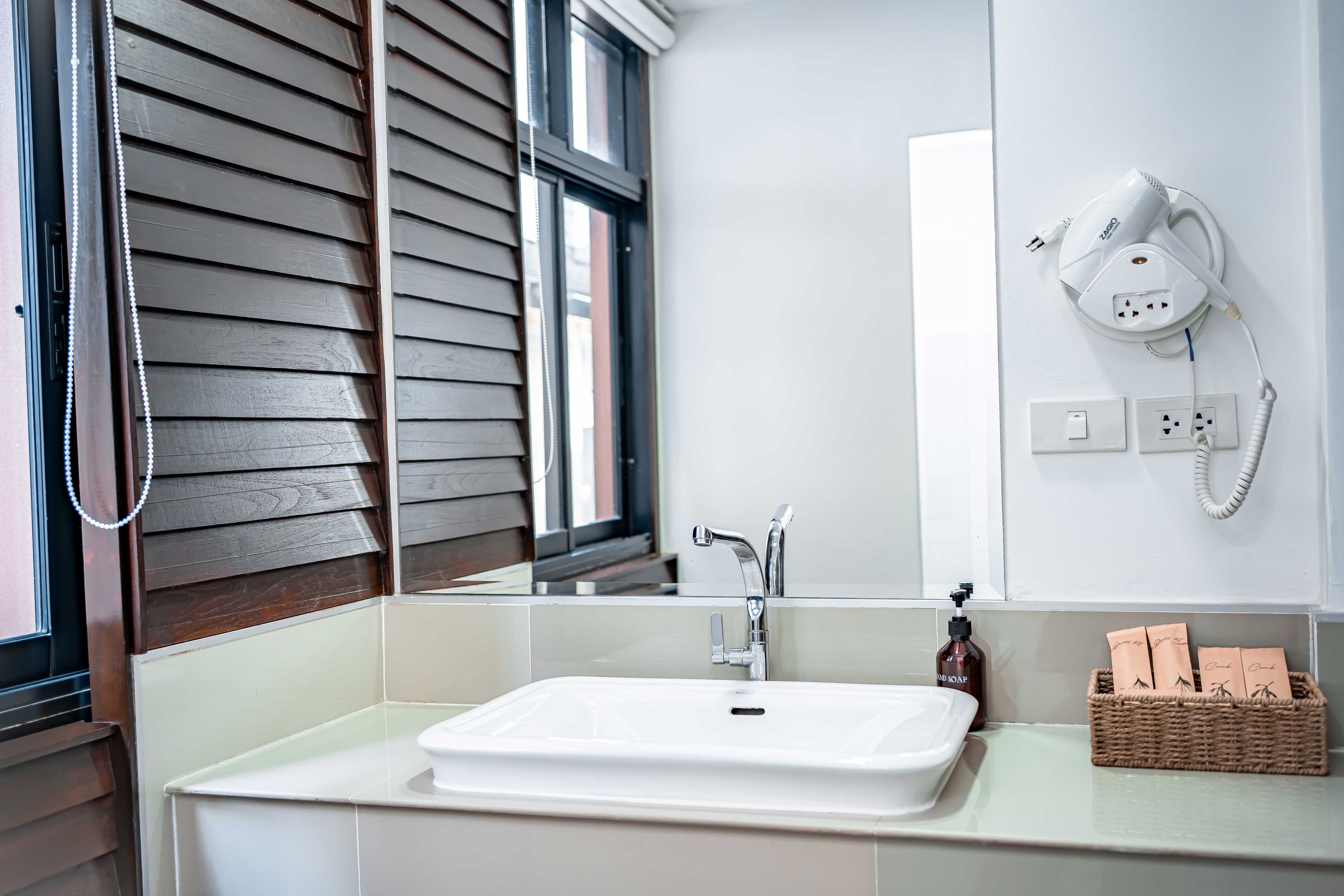 Une salle de bain avec un lavabo blanc, une douchette à main, un téléphone fixé au mur et un panier contenant des articles de toilette.