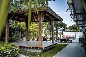 Un espace extérieur abrité, doté de bancs en bois, avec une piscine en arrière-plan.