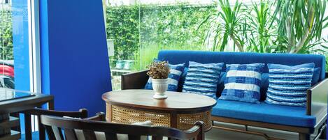 Un sofá azul con cojines a rayas, una mesa redonda de madera con un jarrón blanco y una silla de mimbre.