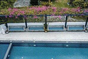 Zona de piscina amb tres gandules blaves i una piscina amb paviment de rajoles blaves.