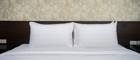 Un lit bien fait, avec du linge de lit blanc et une tête de lit adossée à un mur orné d’un motif de palmiers.