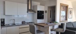A compact kitchen with white cabinets, a stainless steel range hood, a black oven, and a coffee maker.