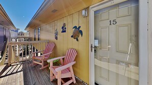 Eine Holzterrasse mit zwei Adirondack-Stühlen, einem kleinen Tisch und einer Tür mit der Nummer 15.