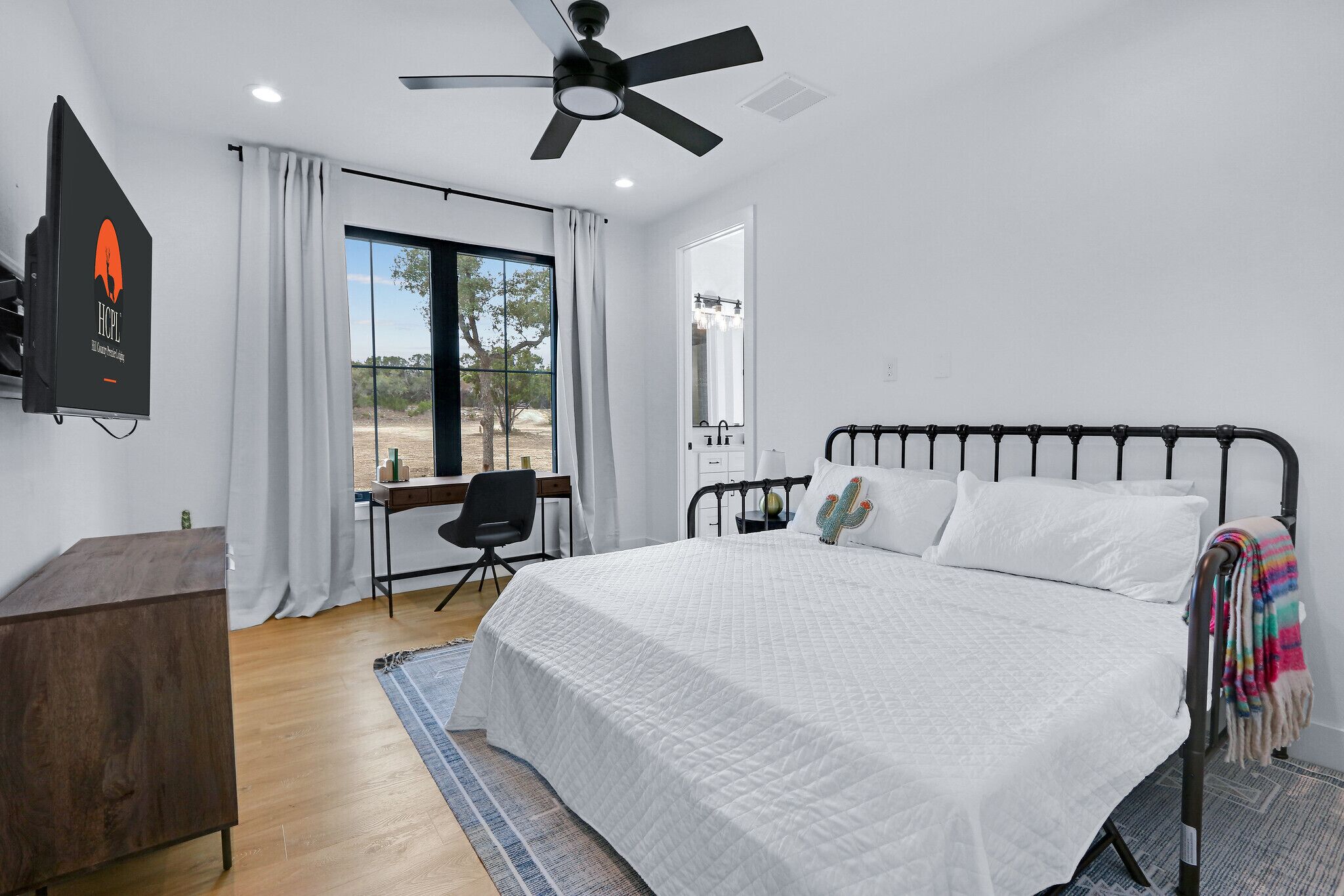 A bedroom with a bed, a desk, a chair, a ceiling fan, and a window with curtains.