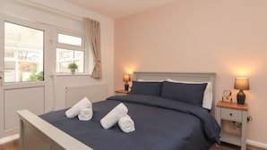 A neatly made bed with two rolled towels, a window with curtains, and two bedside lamps. - Seaside Cottage (Scarborough)