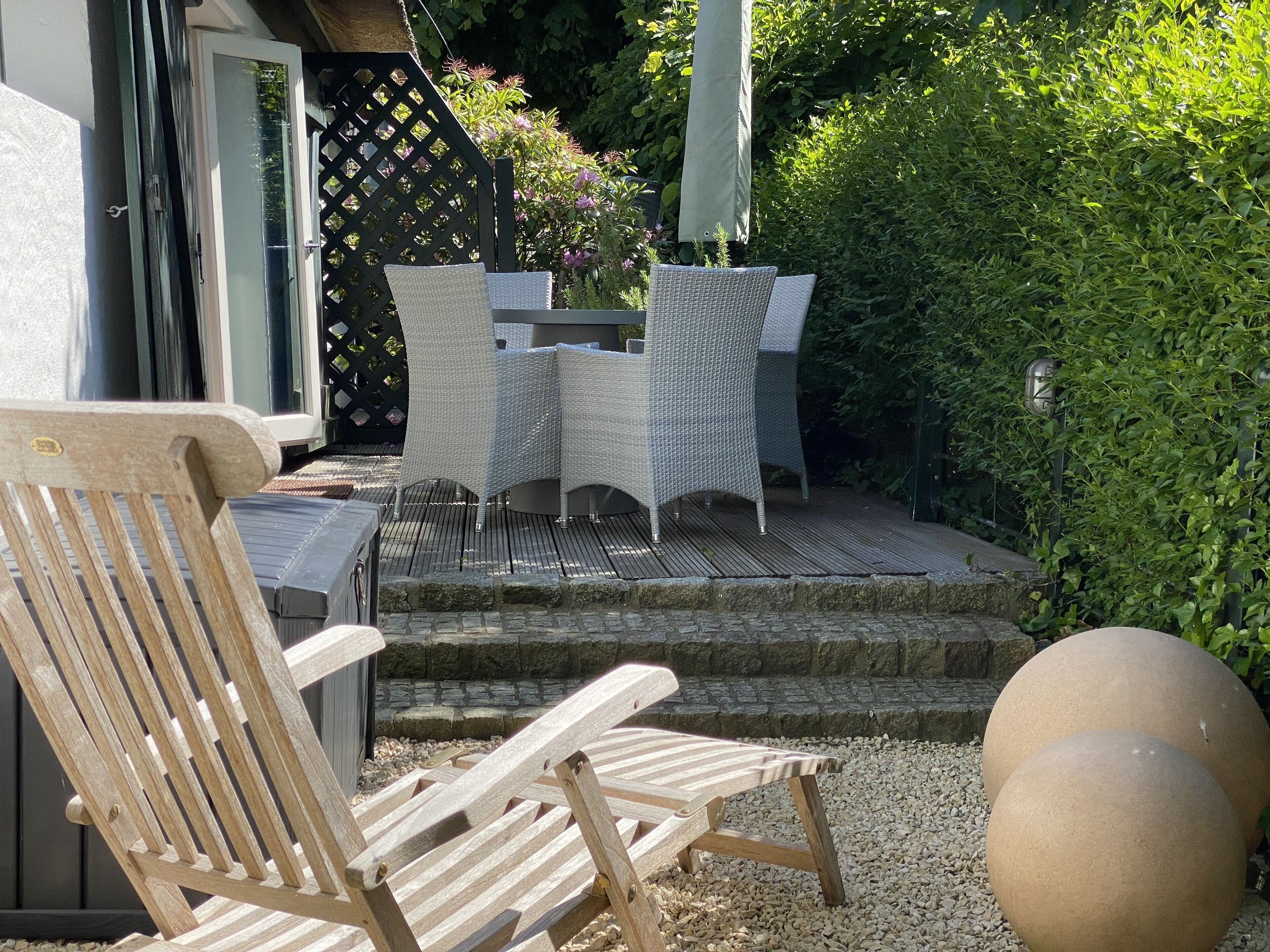 An outdoor patio with wicker furniture, a wooden chair, and a stone wall.