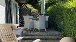 Een terras buiten met rieten meubels, een houten stoel en een stenen muur.