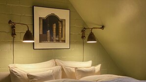 Een slaapkamer met een schuine plafond, een inlijstend schilderij aan de muur, en twee wandlampen.