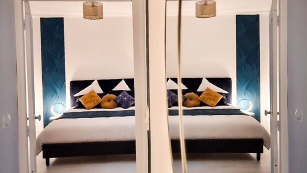 Ein modernes Schlafzimmer mit einem großen Bett, zwei Pendelleuchten und Blick durch eine offene Tür.