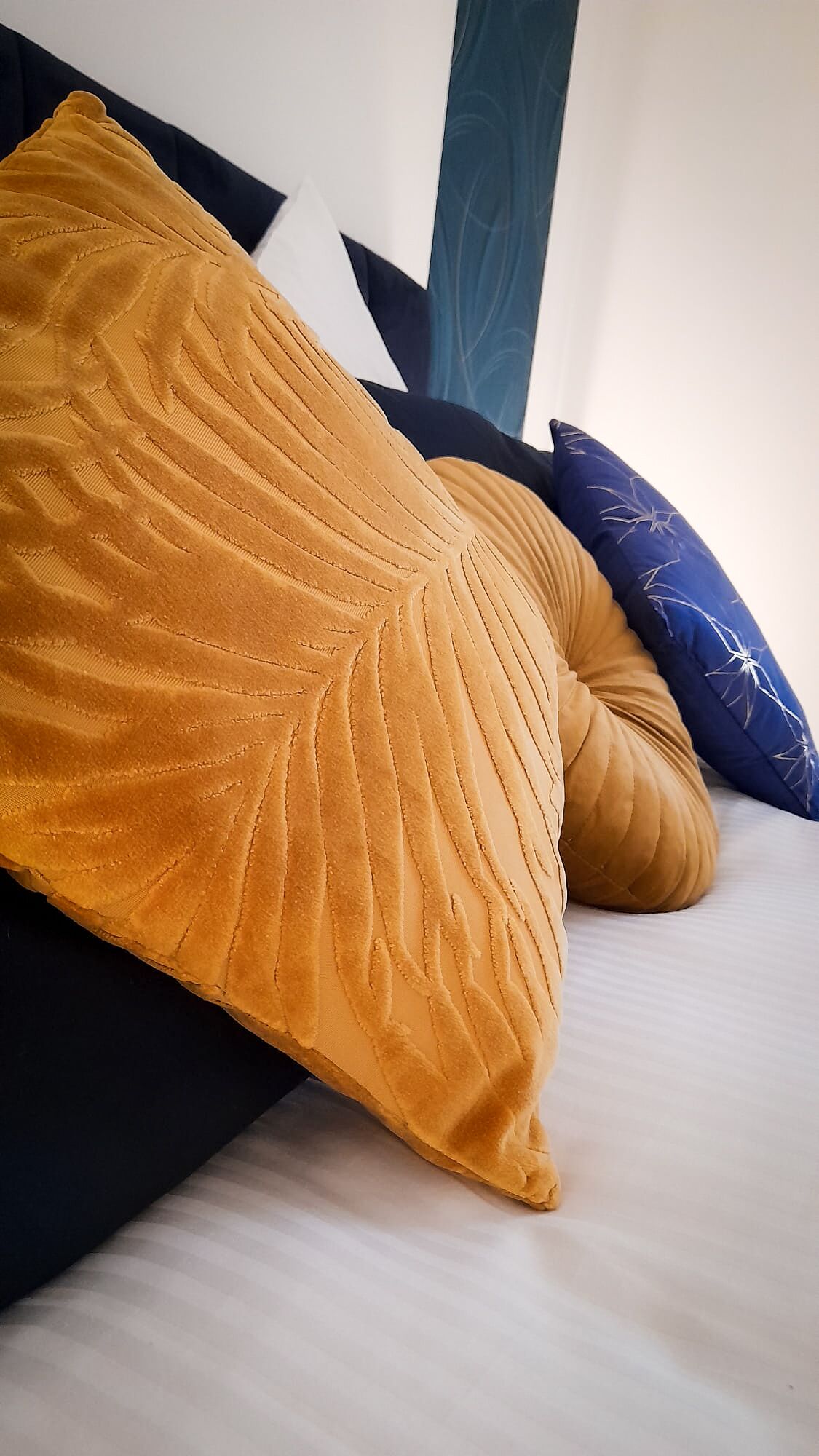 Uma cama com um travesseiro amarelo mostarda e um travesseiro azul com padrão de folha.