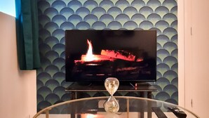 Ein modernes Wohnzimmer mit einem runden Glastisch, einem an einer blauen Wand montierten Flachbildfernseher und einem lindgrünen Vorhang.