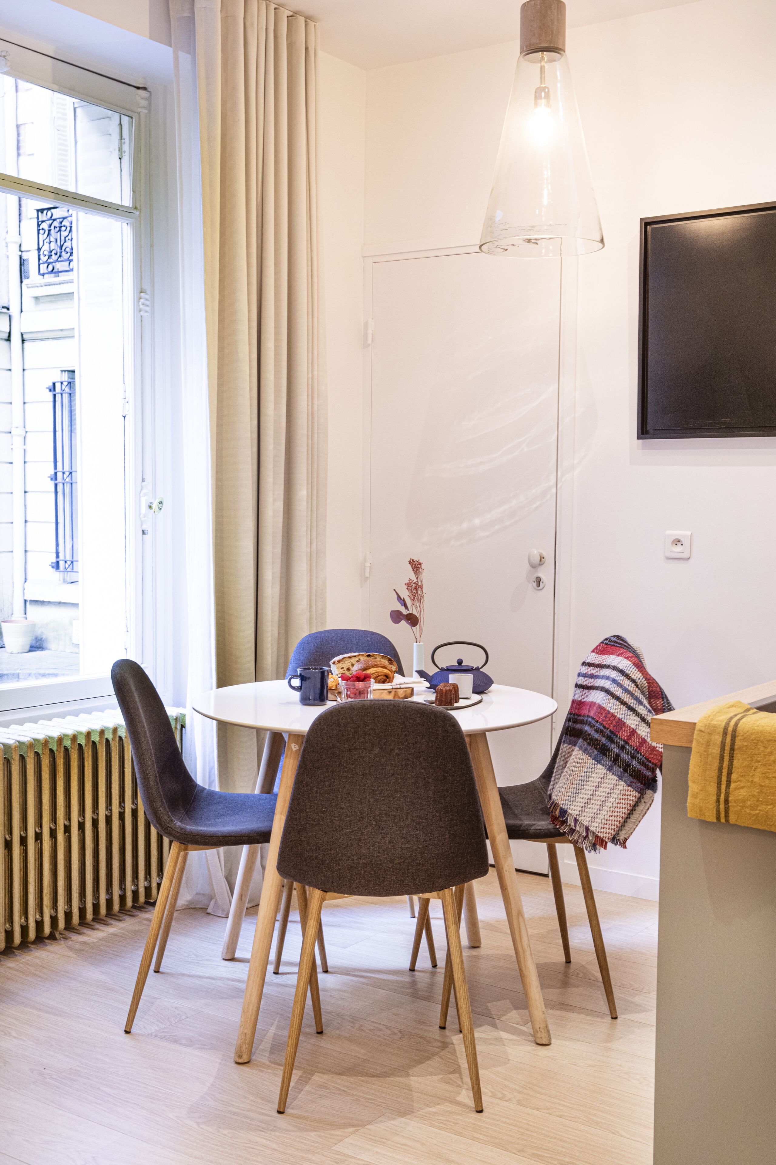 Un coin repas comprenant une table ronde, quatre chaises, un luminaire suspendu et une fenêtre avec des rideaux.