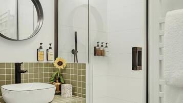 Une salle de bain moderne avec une baignoire sur pieds, un miroir rond, un lavabo agrémenté d’un vase de tournesols et une douche séparée par une paroi de verre.