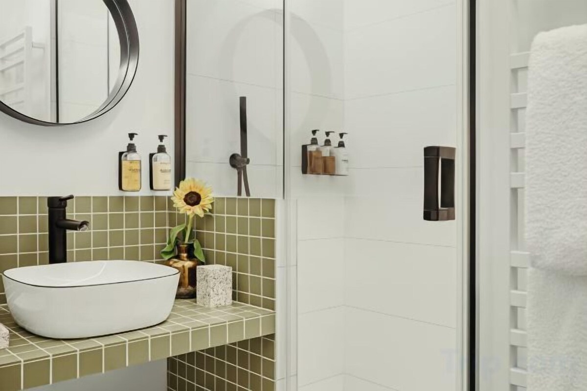 Un bagno con un lavandino bianco, uno specchio rotondo e una zona doccia.