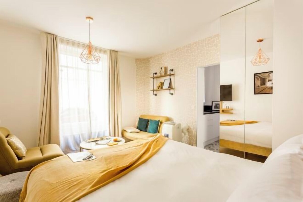 A hotel room with a bed, a desk with a chair, a sofa, a TV, and a wardrobe.