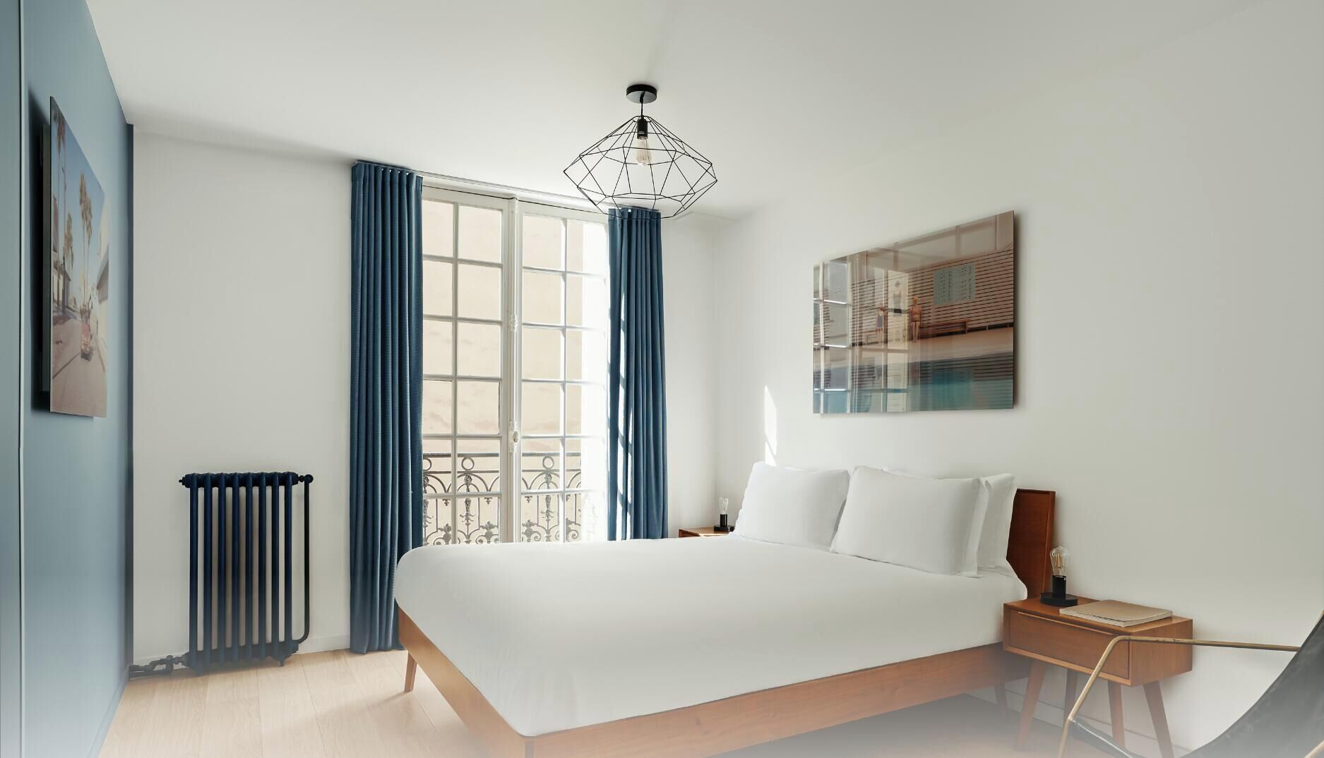 Une chambre moderne avec un grand lit, un radiateur, une fenêtre avec des rideaux, un luminaire suspendu et une œuvre d’art accrochée au mur.