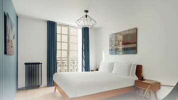 Une chambre moderne avec un grand lit, un radiateur, une fenêtre avec des rideaux, un luminaire suspendu et une œuvre d’art accrochée au mur.