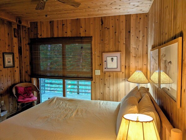A wooden-paneled room with a bed, a chair, a window, and a lamp.