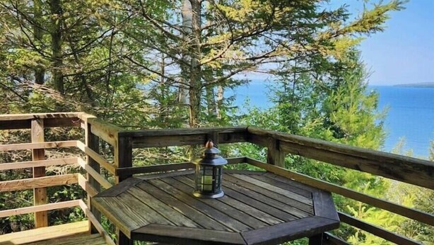 A wooden deck with a table and bench, overlooking a body of water and forested area.