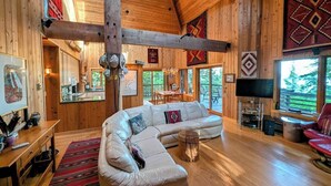 A wooden interior with a large L-shaped sofa, a dining area, and a TV.