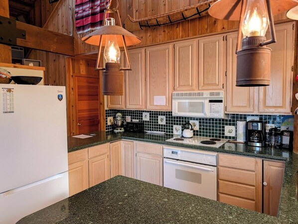A kitchen with wooden cabinets, a microwave, a stove, and a refrigerator. - Bean Ravine - Unique Cabin overlooking Lake Superi (La Pointe)