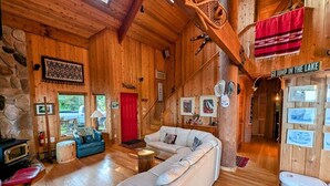 A cozy log cabin interior with a large white sofa, a red door, and a sign that reads 'GO JUMP IN THE LAKE'.