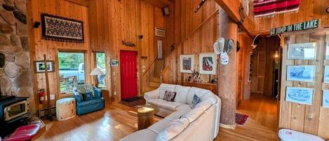 Accogliente interno di una baita in legno con un grande divano bianco, una porta rossa e un cartello con la scritta 'GO JUMP IN THE LAKE'.