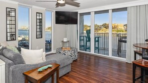A spacious living room with a large sliding glass door leading to a balcony with a view of the sea and buildings. - DP 305B Amazing condo w/Harbor Views (Destin)