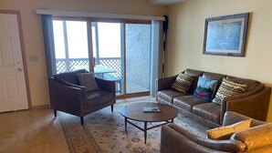 Un salon comprenant un canapé, un fauteuil, une table basse et donnant sur l’extérieur.