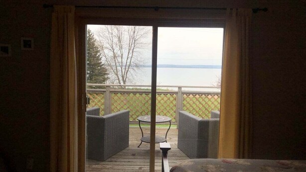Une chambre avec un lit, une fenêtre avec des rideaux, une vue sur une terrasse aménagée avec du mobilier d’extérieur et une table.
