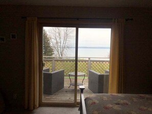 A room with a bed, a window with curtains, a view of a deck with outdoor furniture, and a table. - Parkside Condo 3 - Convenient In Town Condo (La Pointe)