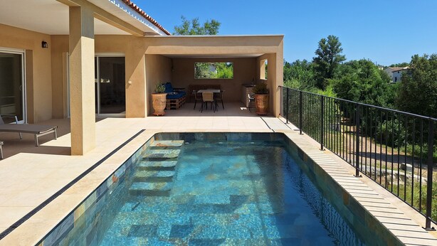 Una piscina con zona de patio, un área de estar techada y vistas al entorno verde.
