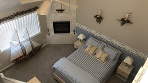 Un dormitorio con cama, mesitas de noche, ventilador de techo, chimenea y un modelo de barco.