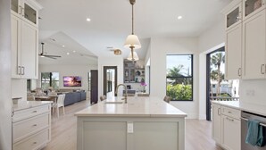 A modern kitchen with a central island, white cabinetry, and pendant lighting. - 🐚Private Pool + Great Outdoor Living Space-Brand New 5BR+Den Home-Funky Conch🐚 (Fort Myers Beach)