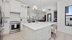 A modern kitchen with white cabinetry, a large island, stainless steel appliances, and a pendant light fixture. - 🐚Private Pool + Great Outdoor Living Space-Brand New 5BR+Den Home-Funky Conch🐚 (Fort Myers Beach)