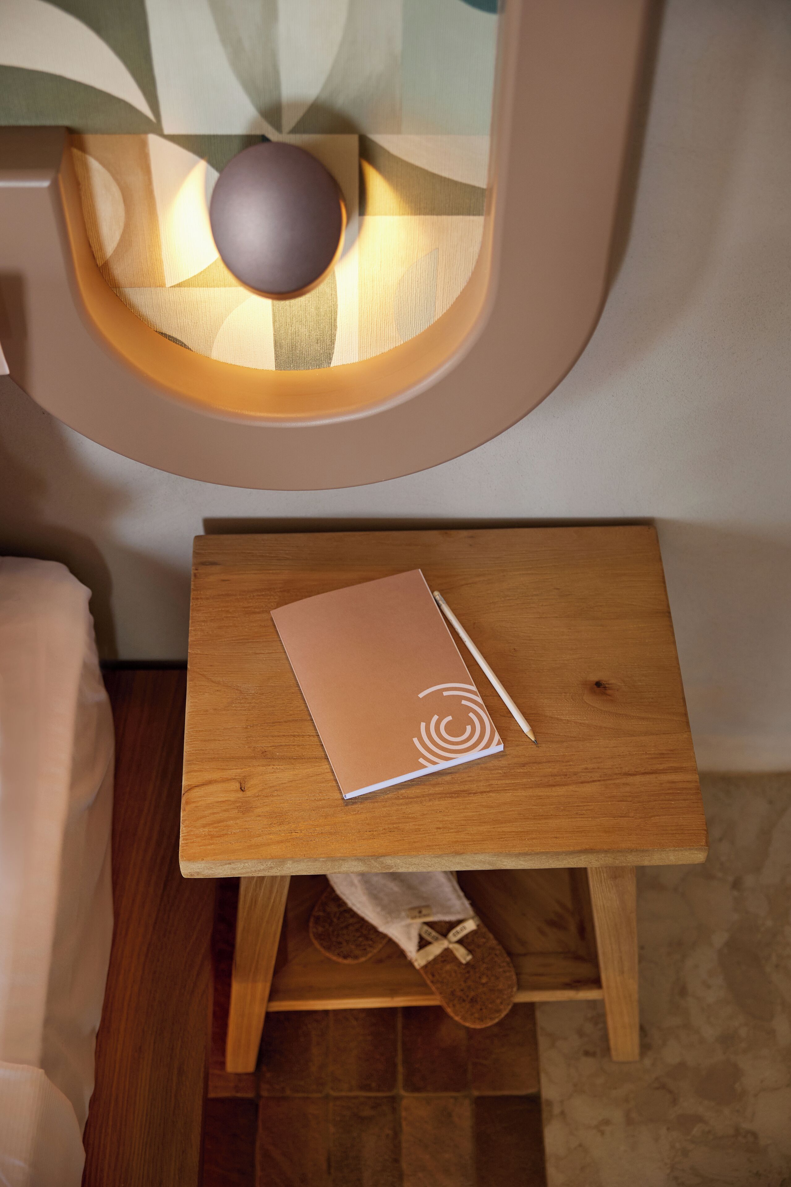 A wooden bedside table with a notebook and pen, a small rug, and a wooden floor.