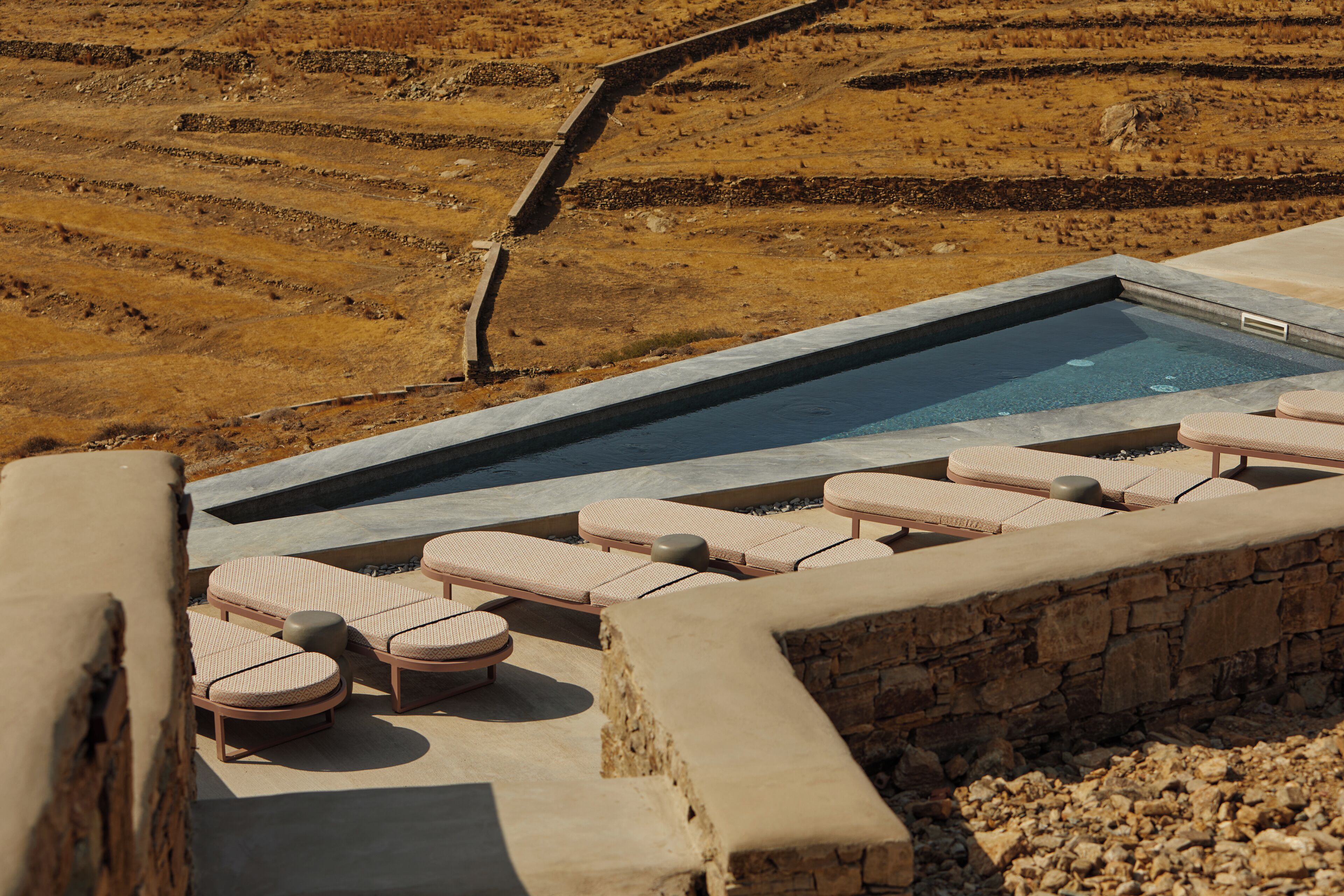 Un área de piscina con sillones de descanso y un muro de piedra.