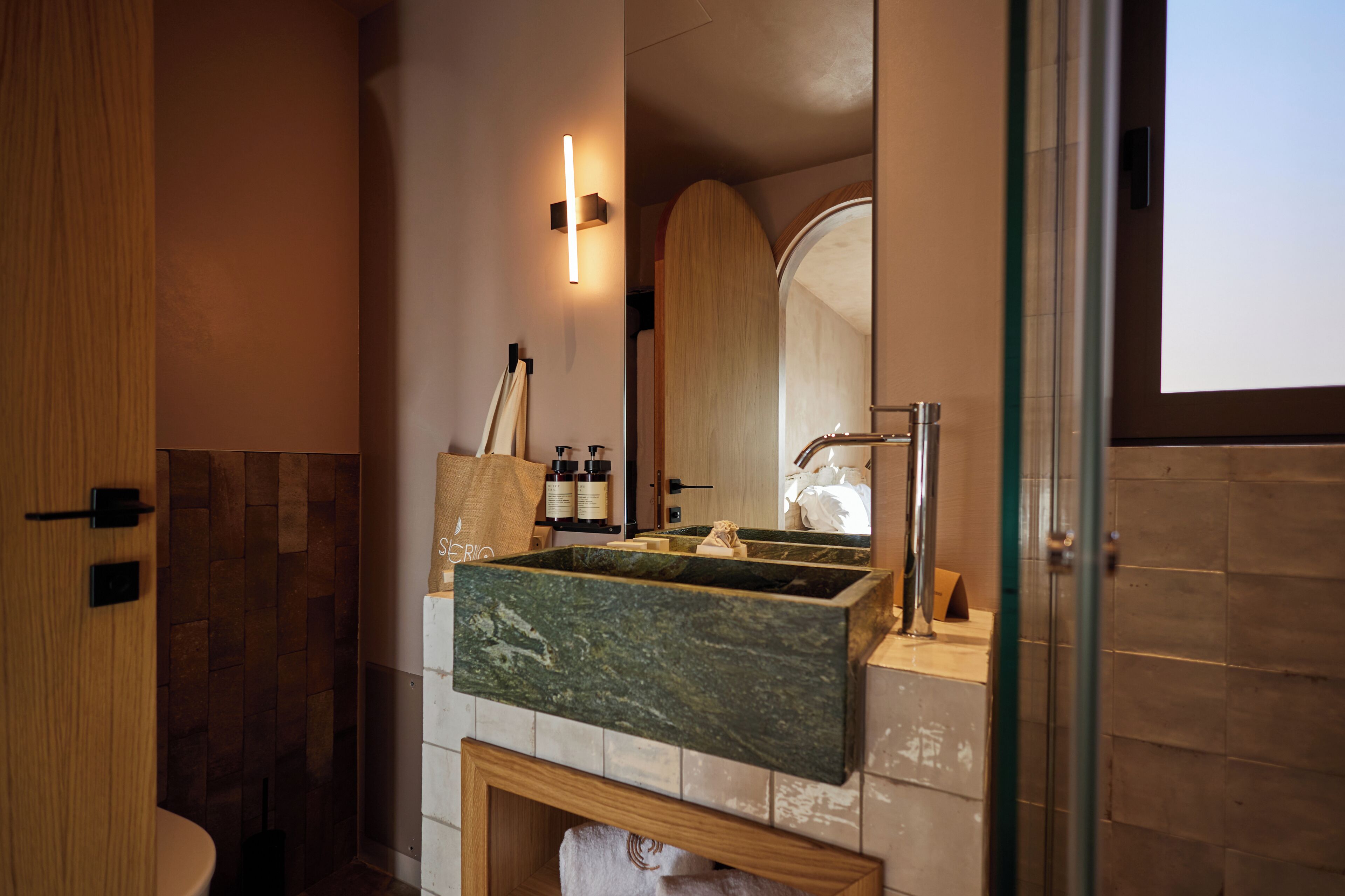 A modern bathroom with a marble sink, a glass shower enclosure, and a wooden door.