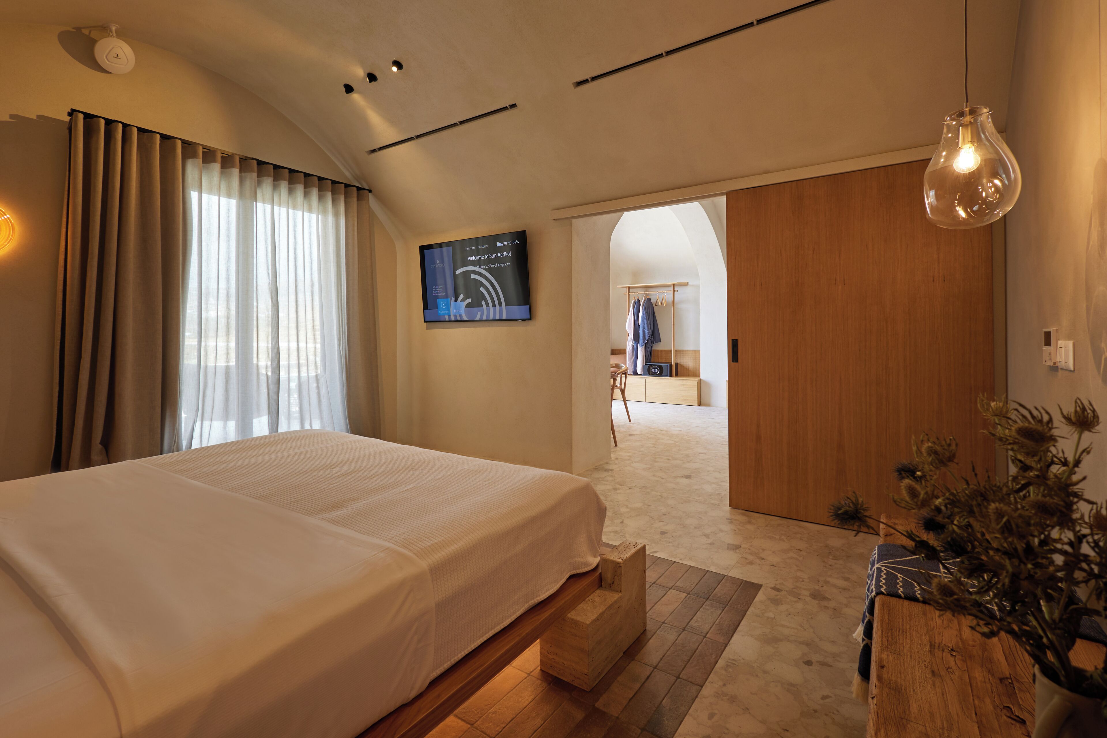 Ett modernt hotellrum med en stor säng, en platt-TV, en garderob i trä och utsikt över korridoren.