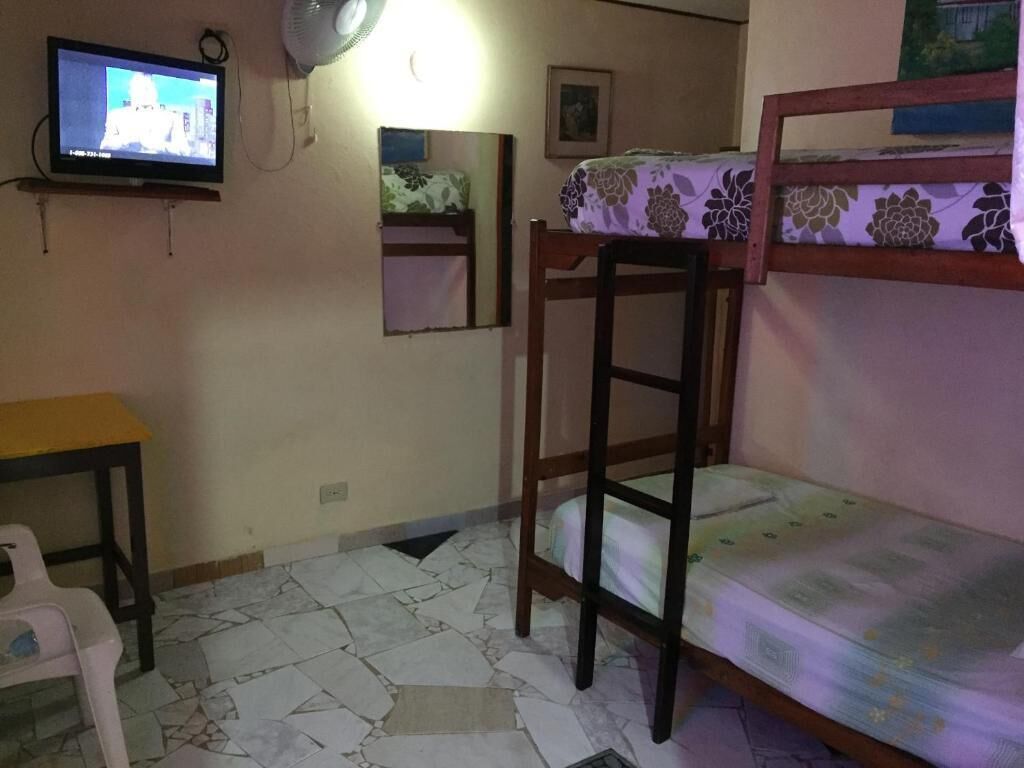 Una habitación con literas, un escritorio, una silla, un televisor, un espejo y una colcha estampada.