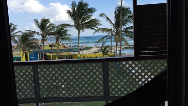 Vista da un balcone su una spiaggia con palme e cielo sereno.