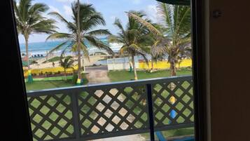 Un balcón con vista a una playa, palmeras y una zona delimitada por una cerca.