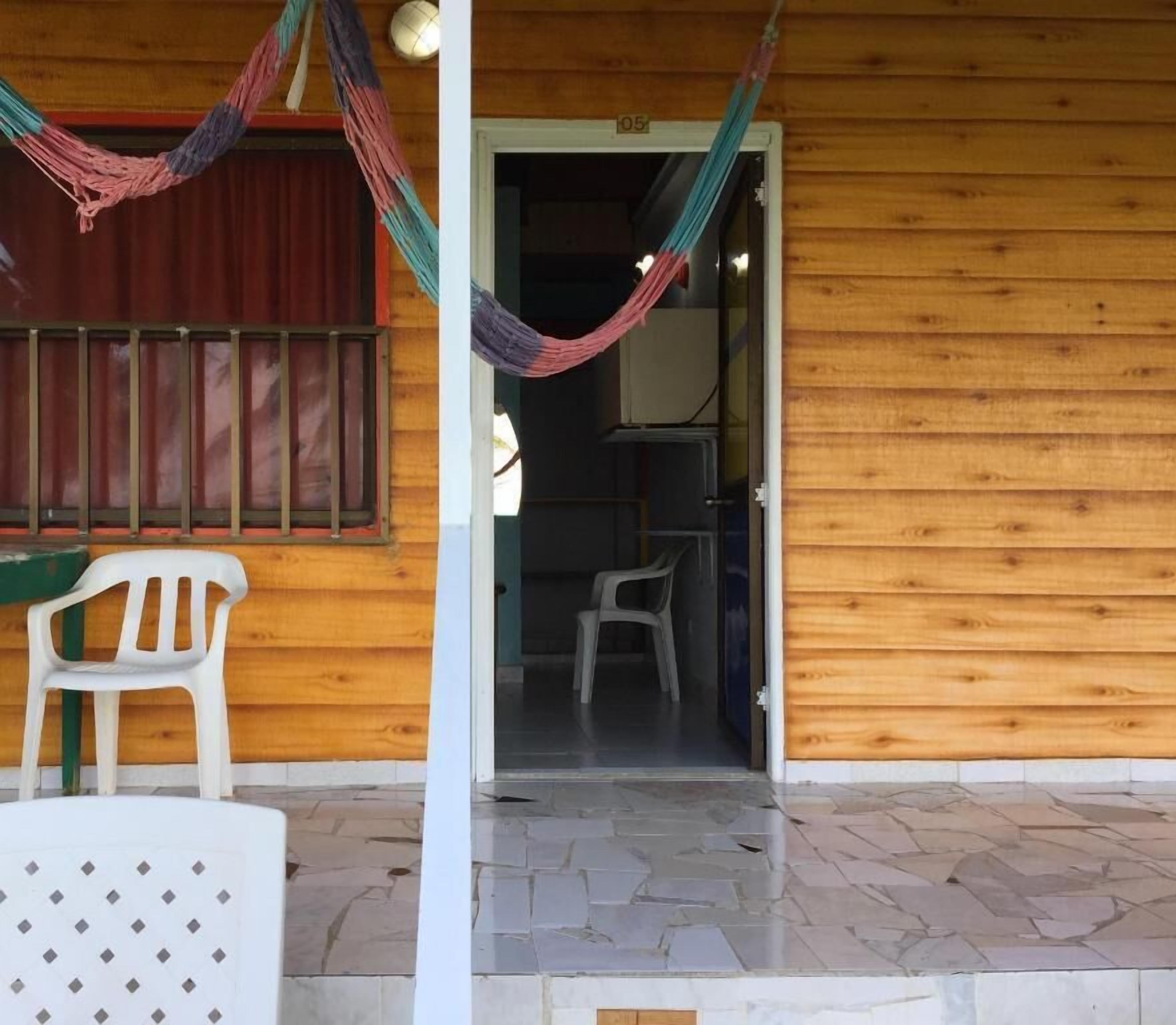 Un edificio de madera con un patio de baldosas, una silla de plástico blanca y una hamaca.